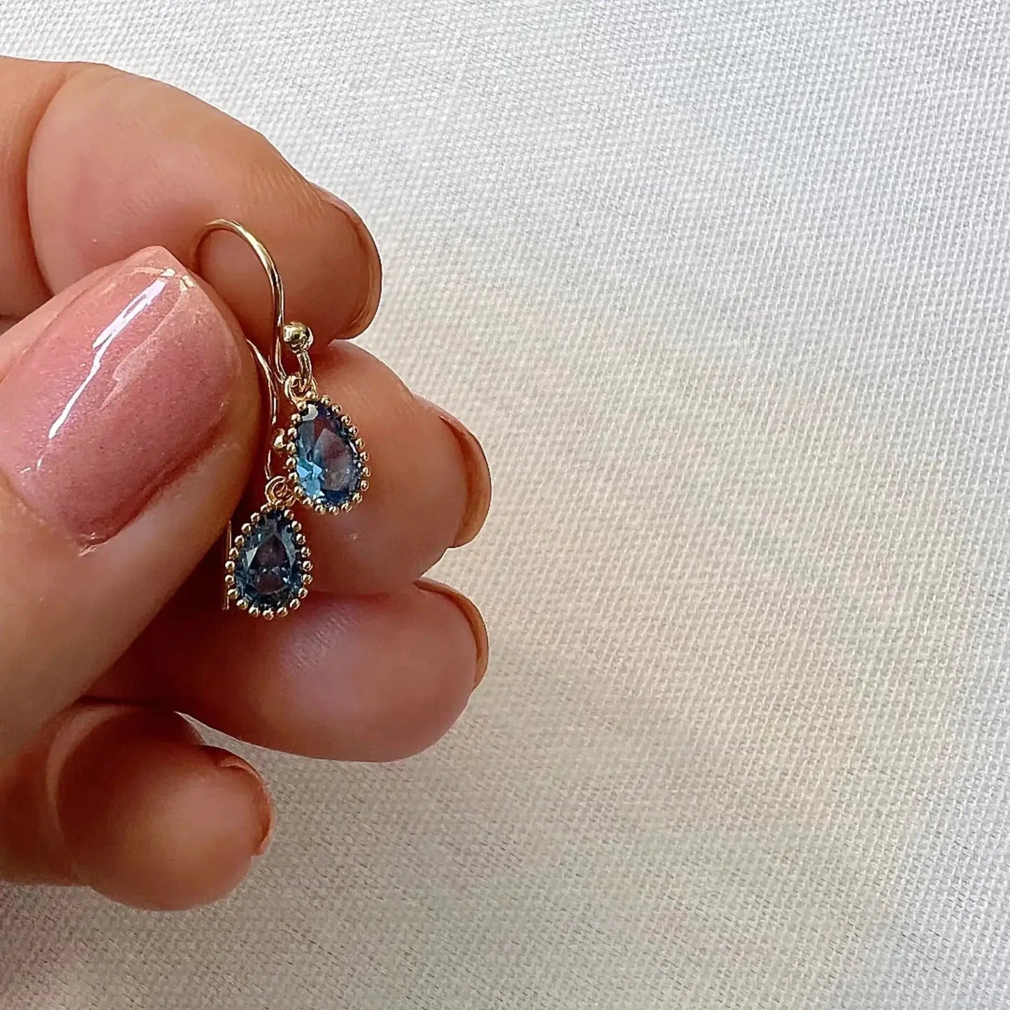 Isla Sapphire Blue Crystal and Gold Earrings showcased on a hand with a light nail polish.