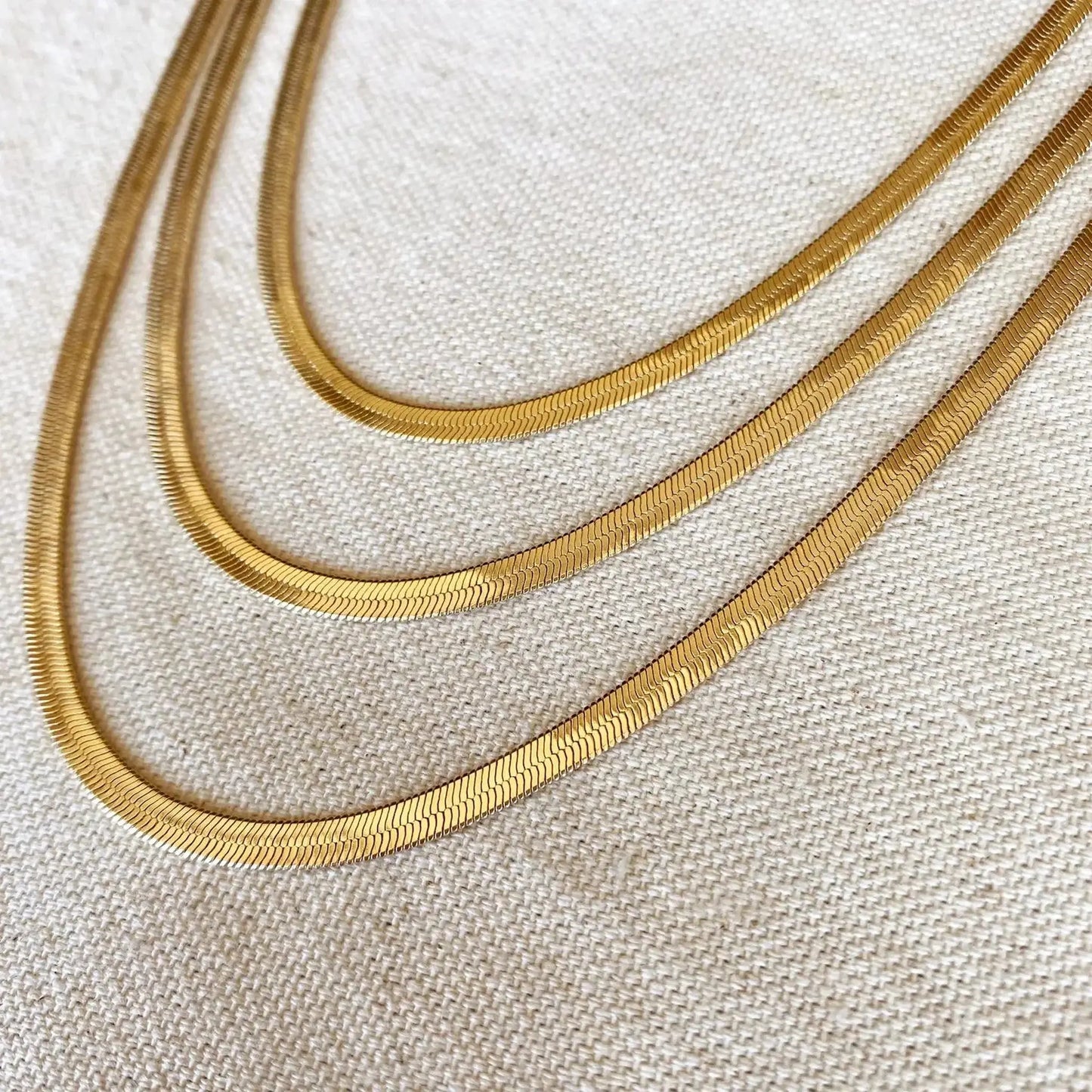 Ashlyn Herringbone Necklace showcasing its flat, interlocking links with a liquid shine on a textured background.
