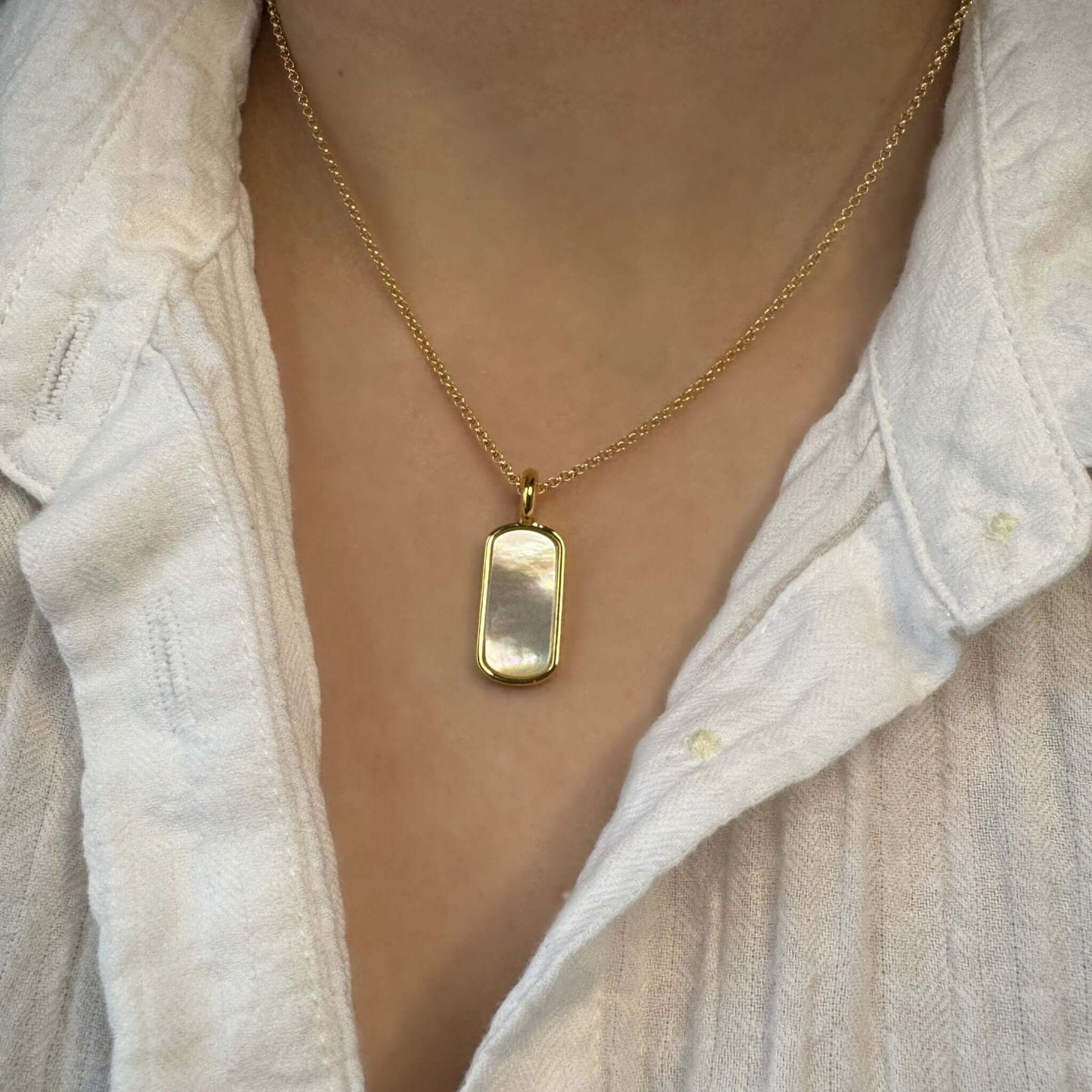 Nellie Mother of Pearl Pendant Necklace hanging on a gold chain, showcasing the iridescent pendant against a white shirt.