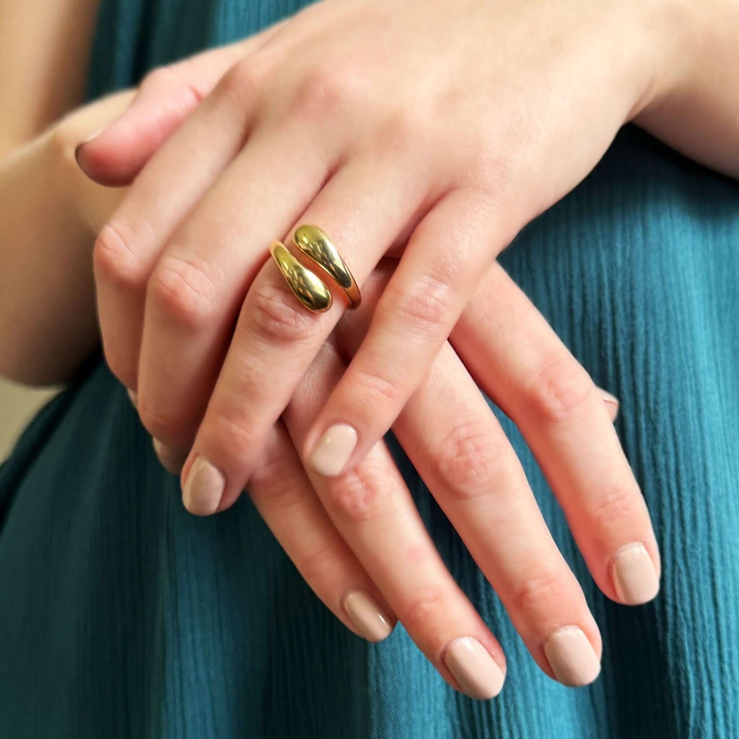 Reagan Adjustable Wrap Ring worn on fingers with polished gold finish against a teal background.