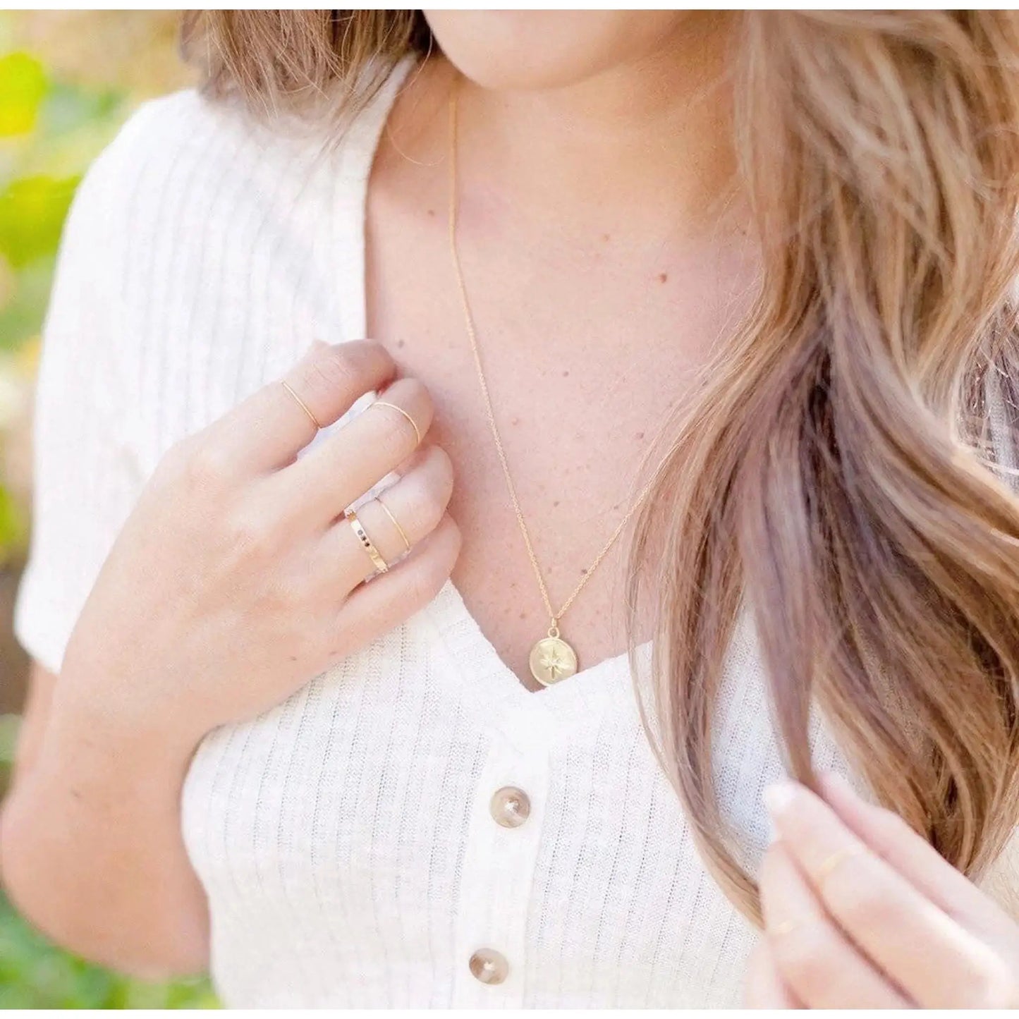 Lyra Starburst Pendant Necklace worn by a woman with layered rings, showcasing its elegance and detailed design.
